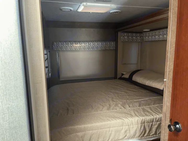 This image shows a cozy RV rental bedroom. A neatly made bed with light brown bedding and a pillow suggests comfort for your travels.. Forest River Sunseeker 2016