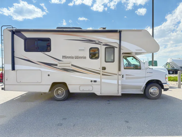 Side view of a clean, light-colored Winnebago Minnie Winnie RV rental on asphalt under a blue sky.. Winnebago Minnie Winnie 2016