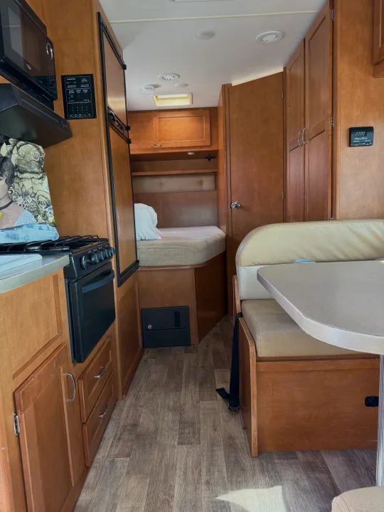RV rental interior: kitchen with stove, microwave, fridge; dinette, and bunk bed. Shows living area, controls, and utility panel.. Winnebago Minnie Winnie 2016