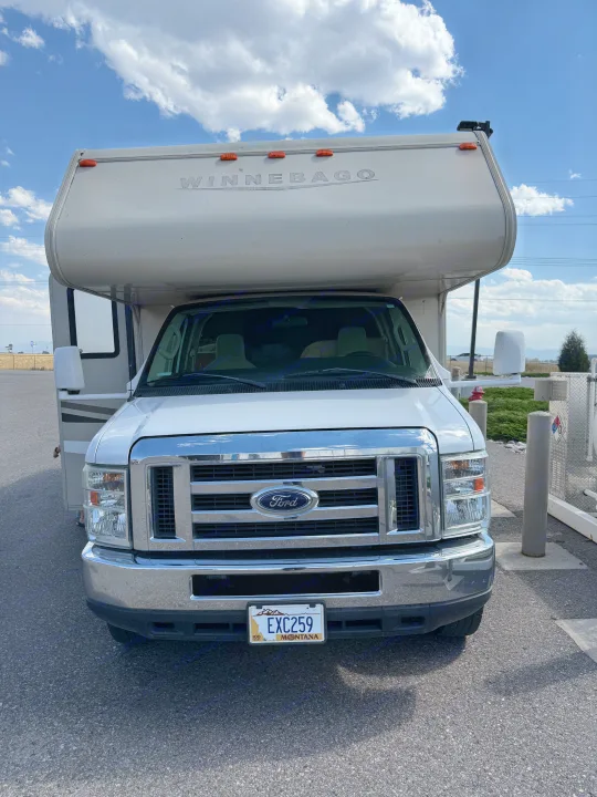 Front view of a white Winnebago Class C RV rental, Ford-based, parked under a bright sky with clouds. Montana license plate visible.. Winnebago Minnie Winnie 2016