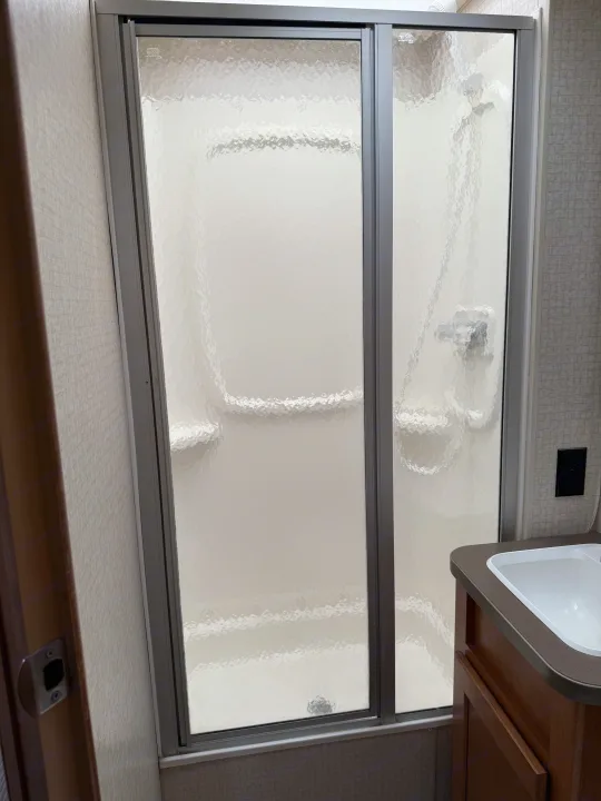 RV rental bathroom interior: A functional space featuring a compact shower with frosted glass doors and an adjacent vanity with sink.. Winnebago Minnie Winnie 2016