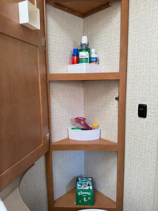 RV rental storage: Corner cabinet shelves stocked with toiletries like mouthwash, razor, and Kleenex in a compact space.. Winnebago Minnie Winnie 2016
