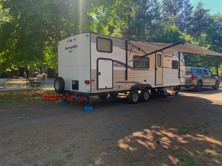 Springdale RV rental travel trailer set up at a sunny campsite, hitched to a gray pickup truck, ready for outdoor adventure.. Keystone RV Springdale 2019