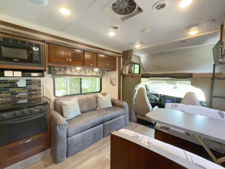 RV rental: Bright interior showing kitchen, sofa, dining booth, and driver's area with overhead bunk.. Forest River Sunseeker 2017