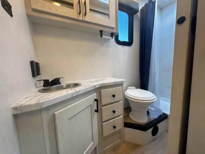 Compact RV rental bathroom showcasing a corner sink vanity, toilet on a raised base, and a walk-in shower.. Nexus Other 2026
