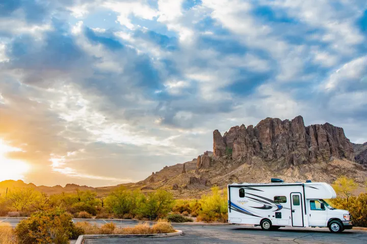 White RV rental at sunset amidst rugged Superstition Mountains, Arizona. Stunning desert landscape & vibrant clouds.. Nexus Other 2026