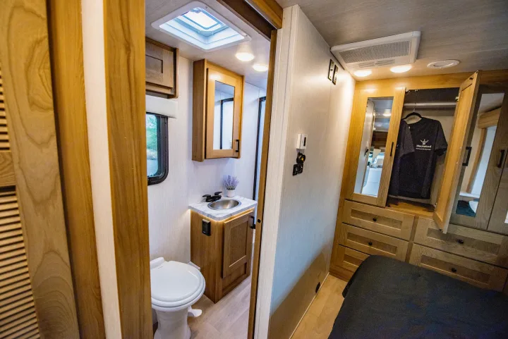 RV rental interior showing a compact bathroom with sink and toilet, and a bedroom area with wooden storage and a closet.. Nexus 29T 2026