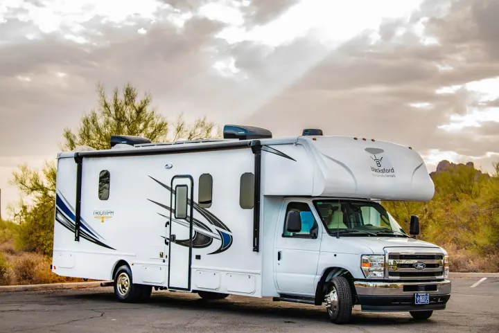 A white Class C RV rental from Blacksford, parked in a desert landscape under a cloudy sky. Perfect for outdoor travel.. Nexus Other 2026