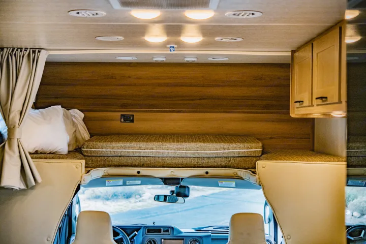 Cozy RV rental interior with bunk bed over the driver's cab, showing sleeping area, curtains, and dashboard view.. Nexus Other 2026
