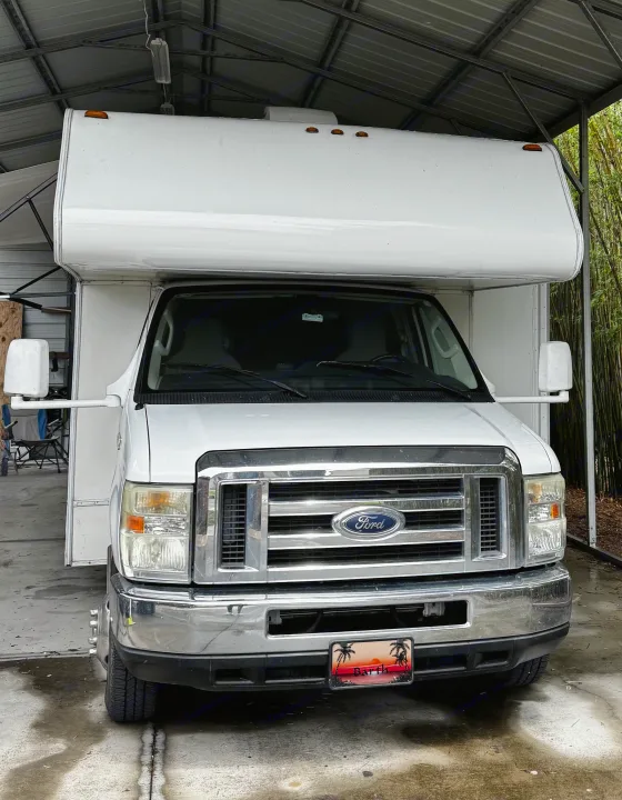 White Ford Class C RV rental, featuring an over-cab bunk, parked under a metal carport.. Forest River Coachmen Freelander 2011