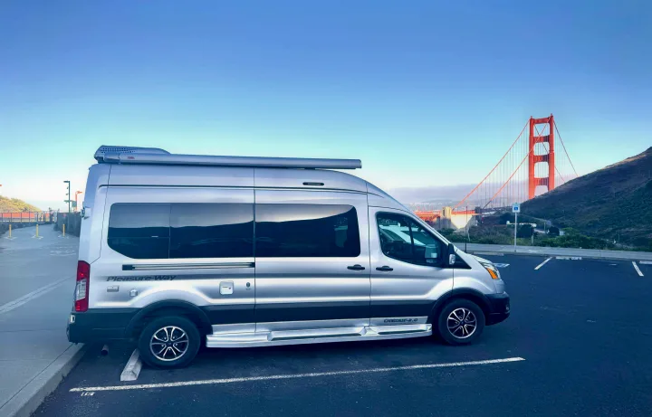Silver Pleasure-Way RV rental parked with the iconic Golden Gate Bridge and hills in the background under a clear sky.. Pleasure-Way Pleasure-Way Class B 2023