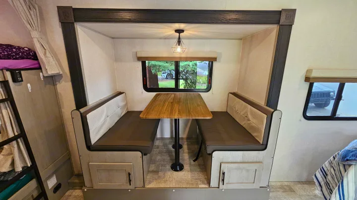 RV rental dinette: a comfy, compact space with light-toned benches, a wooden table, and an overhead light, perfect for meals.. Forest River Ibex 2024