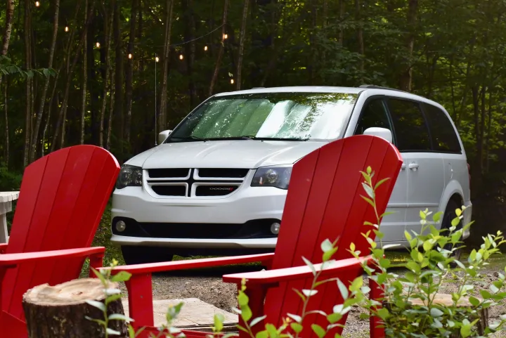 White Dodge minivan, often used for camping, parked in a forest by red chairs. Consider it for your RV rental adventure.. Dodge Dodge Grand Caravan GT 2017 2017