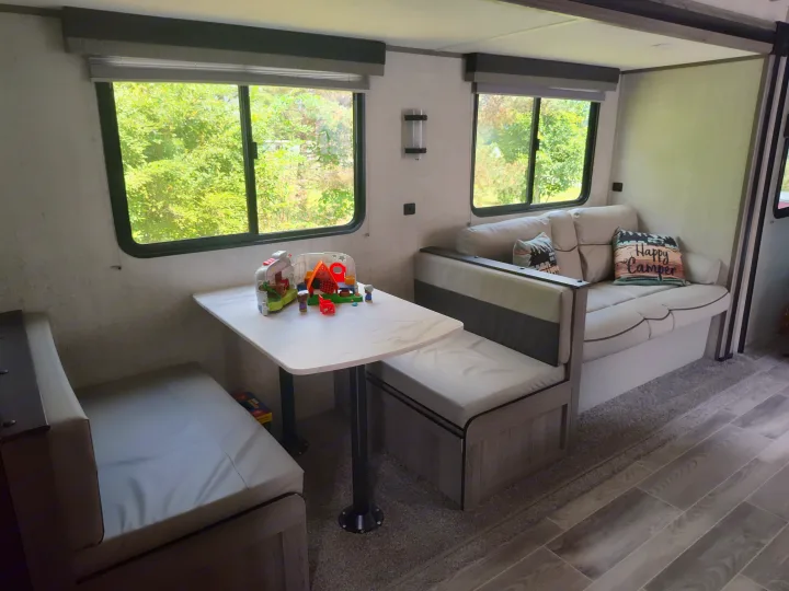Cozy RV rental interior with dining area, sofa, and windows showing nature. Perfect for your next adventure!. Gulf Stream Ameri-Lite 2021