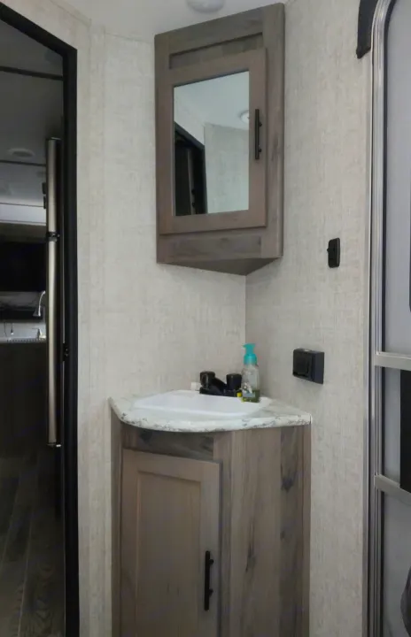 Inside an RV rental: a compact bathroom featuring a corner sink, black faucet, and mirrored medicine cabinet for small spaces.. Gulf Stream Ameri-Lite 2021