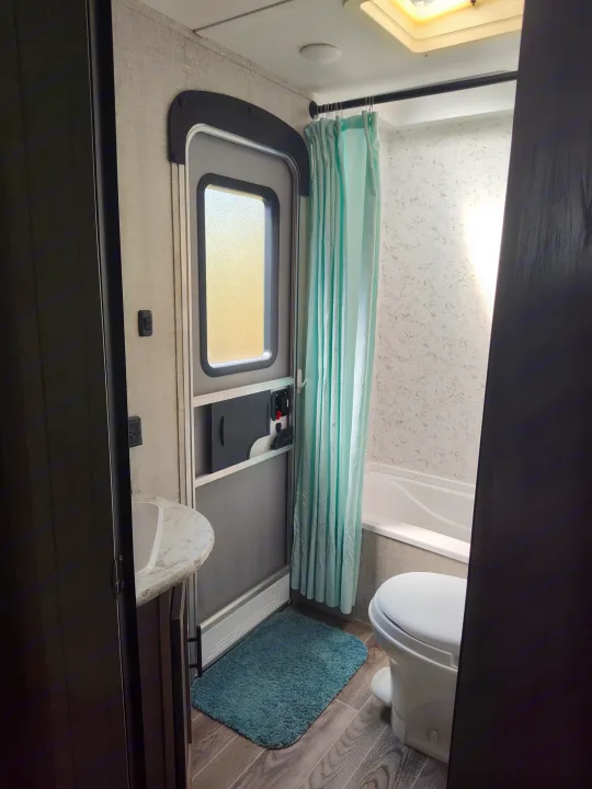 Compact RV rental bathroom features a sink, toilet, and shower with a blue curtain, perfect for travel comfort.. Gulf Stream Ameri-Lite 2021