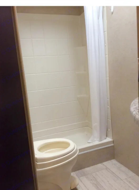Compact RV rental bathroom: toilet, white tiled shower stall with curtain, and wood-look floor.. kz 26' SPORTSMAN 2018