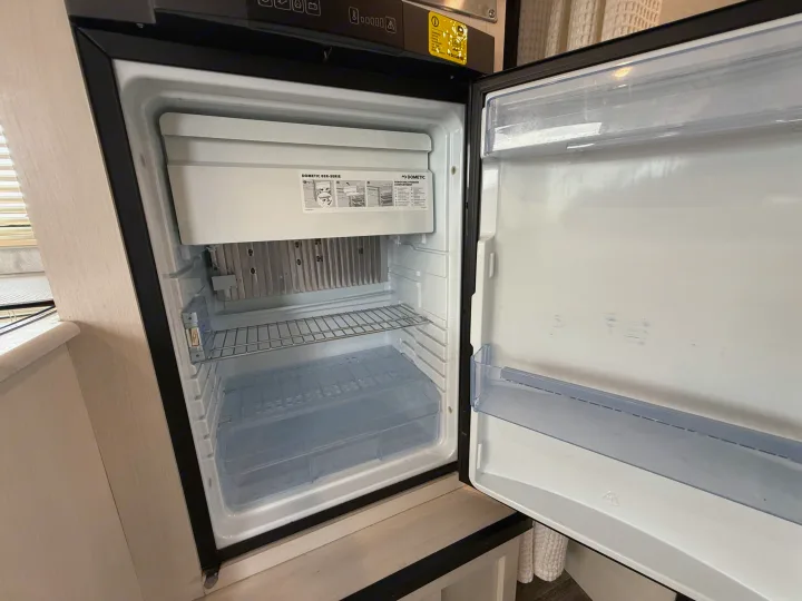 The compact Dometic refrigerator in an rv rental is open, showing its empty freezer, wire shelf, and clear crisper.. R-Pod R-Pod Trailer 2021