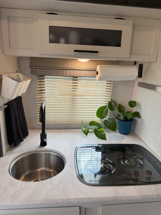 Compact RV rental kitchen features a sink, black faucet, 2-burner Suburban stove, white cabinets, blinds, and a plant.. R-Pod R-Pod Trailer 2021