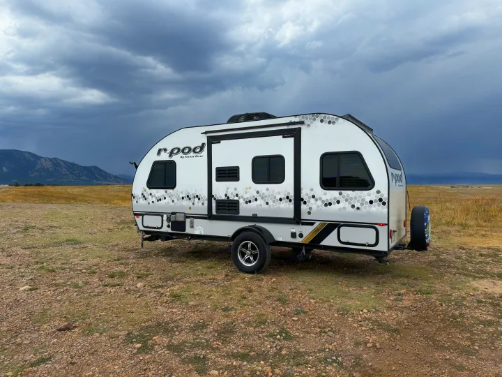 An r-pod travel trailer (RV rental) sits in a dry field under dark, cloudy skies, with mountains behind.. R-Pod R-Pod Trailer 2021