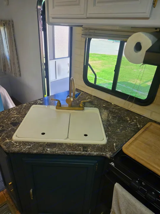 RV rental: Bright, renovated kitchen with a covered sink, brass faucet, dark cabinets, stove, and outdoor view.. Keystone RV Passport Grand Touring 2015