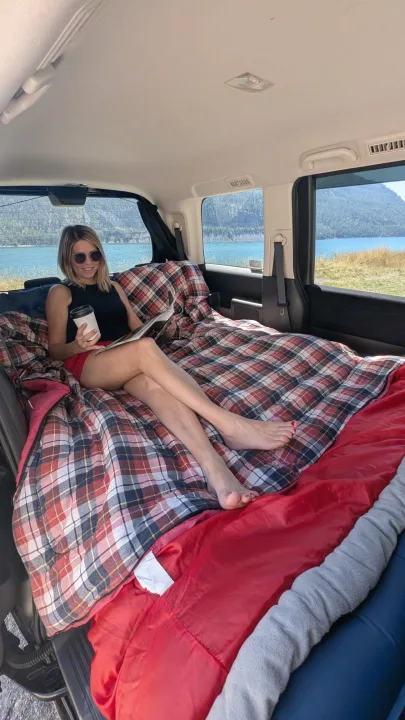 Scenic rv rental setup! A woman relaxes with coffee & a magazine in a cozy plaid bed, enjoying lake & mountain views.. Universal Transformer 2009