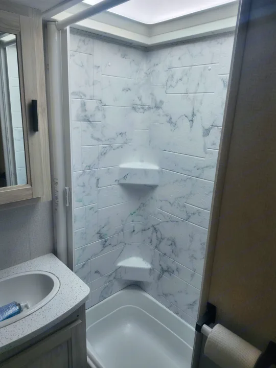 Clean RV rental bathroom: marble-look shower with shelves, compact tub, and vanity sink. Ready for your adventure.. Forester LE 2023