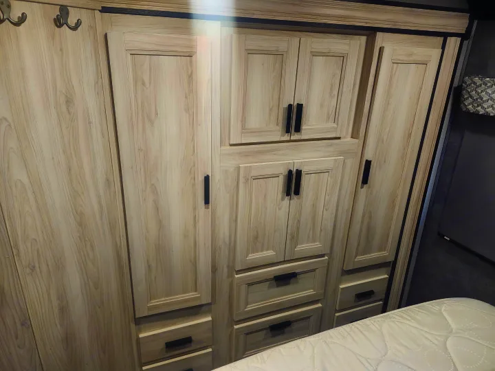 RV rental interior featuring light-toned wooden cabinetry with black handles, ample drawers, and closet space next to a comfortable bed.. Forester LE 2023