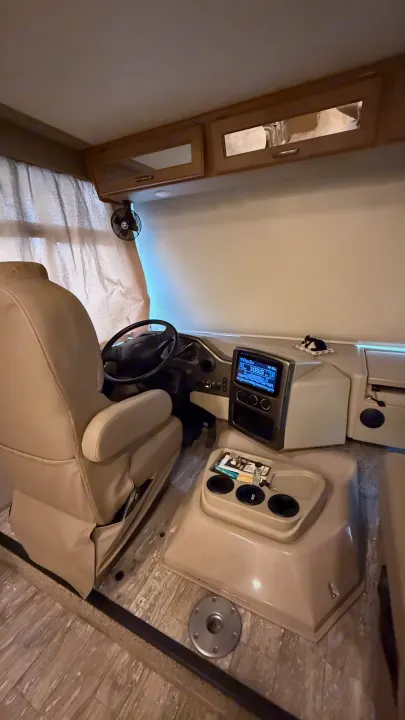 Step inside this RV rental's cockpit, featuring a tan driver's seat, dashboard, and media display.. Thor Hurricane 2019