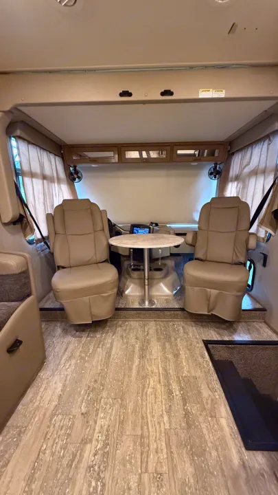 Spacious RV rental interior showcasing the front cabin with driver/passenger seats, a table, and light wood-style flooring.. Thor Hurricane 2019