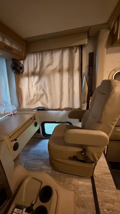 RV rental interior: comfy passenger chair, curtained window, small fan, and wood-look flooring.. Thor Hurricane 2019