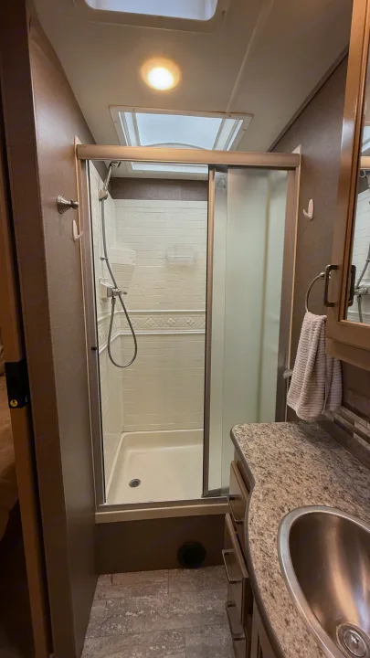 RV rental bathroom with a glass-enclosed shower, stone-look vanity, and stainless steel sink.. Thor Hurricane 2019