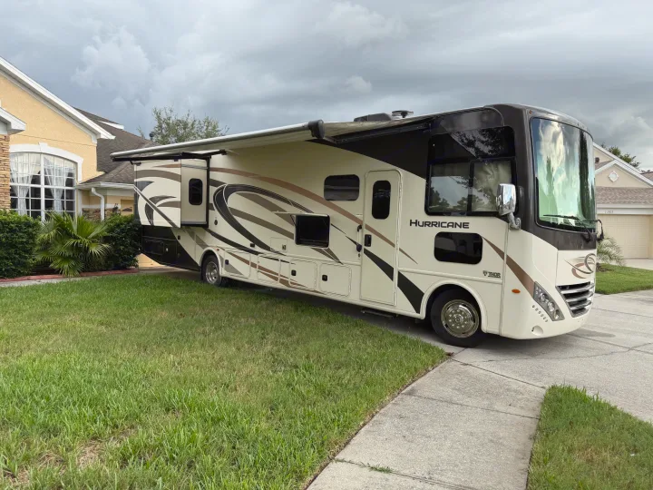 Spacious cream and brown Thor Hurricane RV rental, parked on a driveway beside a house. Awning extended, ready for travel.. Thor Hurricane 2019