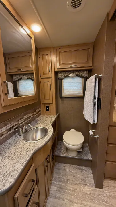RV rental bathroom features a compact design with sink, mirror, toilet, and ample storage cabinets for comfort.. Thor Hurricane 2019