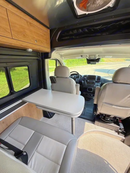 Explore this RV rental's cozy camper van interior with swivel seats, dining table, and overhead storage.. Airstream Airstream Class B 2023