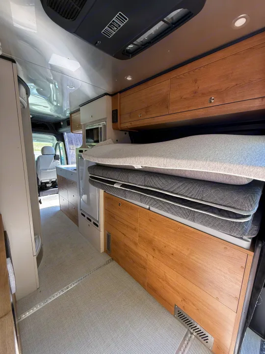 Inside an RV rental camper van: light wood interior, modern kitchen, and a cleverly stowed bed for comfortable travel.. Airstream Airstream Class B 2023