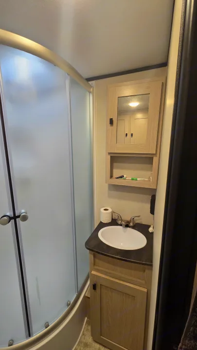 RV rental bathroom features a compact curved shower, vanity with sink, and mirrored medicine cabinet.. Coachmen Apex 2023