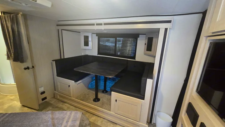 Spacious RV rental dinette area: U-shaped booth with black seating, table, & light wood cabinets. Comfortable travel setup.. Coachmen Apex 2023