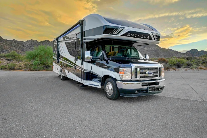 A black and white Entegra motorhome, perfect for rv rental, parked against a scenic backdrop of mountains and desert flora.. Entegra Esteem 2025