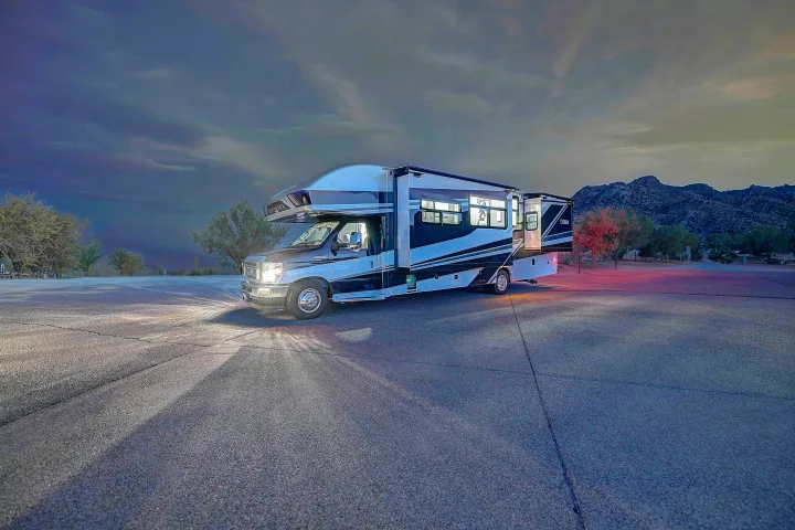 Nighttime view of a sleek RV rental parked on asphalt, lights glowing, mountains & trees in background. Ready for adventure.. Entegra Esteem 2025