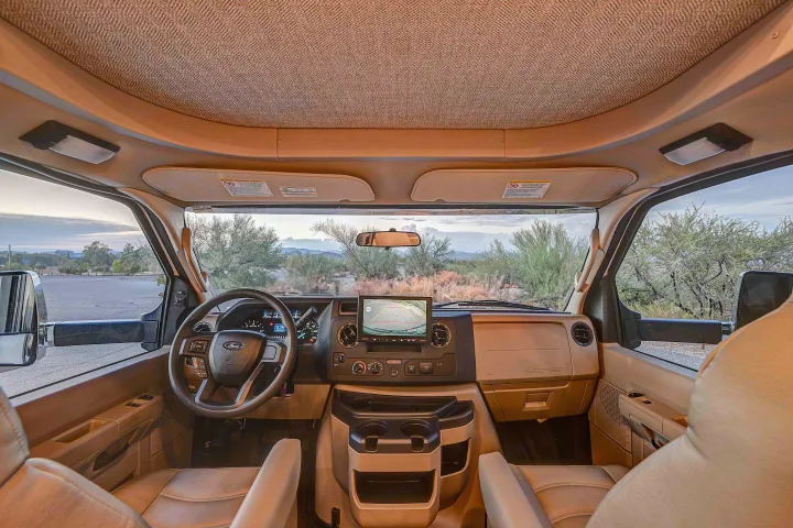 Step into this RV rental's driver's cockpit, featuring a dashboard, steering wheel, and a clear desert view.. Entegra Esteem 2025