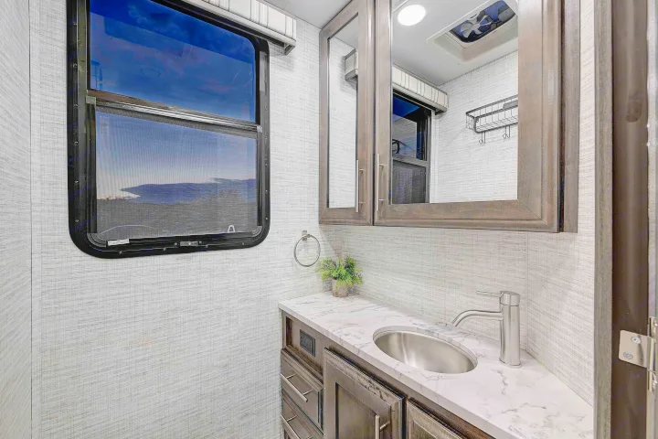 Modern RV rental bathroom interior showcasing a vanity with sink, mirror, and window view. Includes cabinet storage.. Entegra Esteem 2025