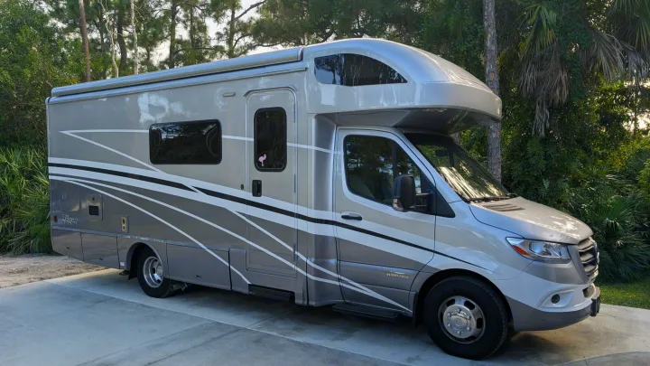 Grey and white rv rental motorhome parked on a driveway with green trees in the background.. Winnebago View 2025