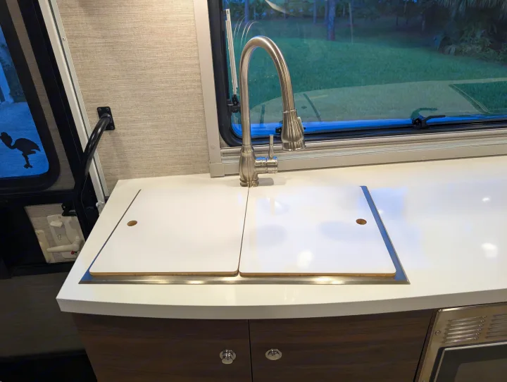 RV rental kitchen: Clean countertop with sink covers, modern faucet, & nature view window.. Winnebago View 2025