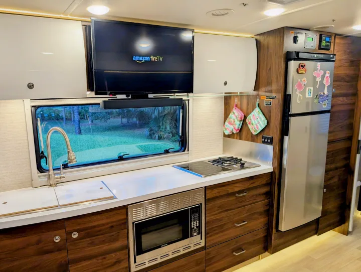 Bright RV rental kitchen with built-in appliances, TV, and a scenic window view. Functional and comfortable.. Winnebago View 2025