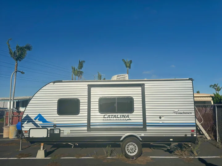 A silver and blue Coachmen Catalina Summit Series travel trailer RV rental, parked under a clear blue sky, visible from the side.. Coachmen Catalina Summit Series 7 2022