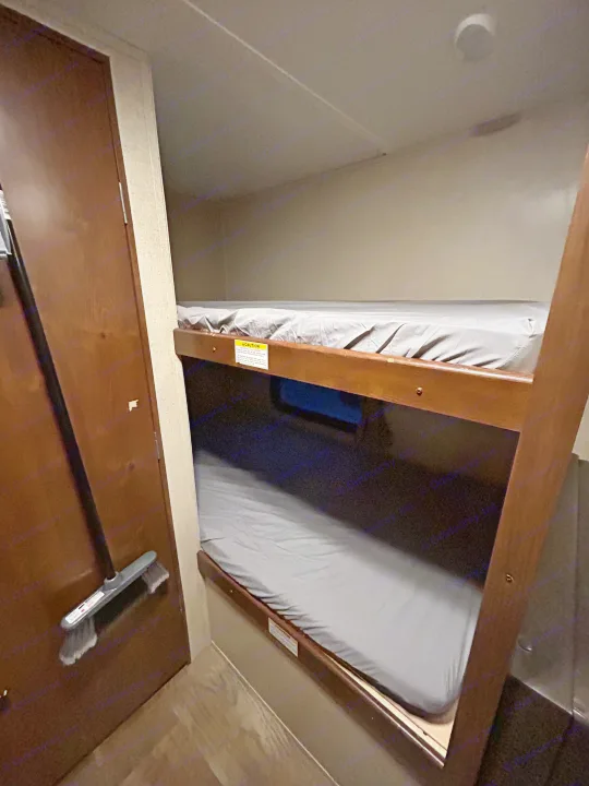 RV rental bunk bed sleeping area with two beds, grey sheets, and a broom by the adjacent door.. Crossroads RV Z-1 Lite 2017