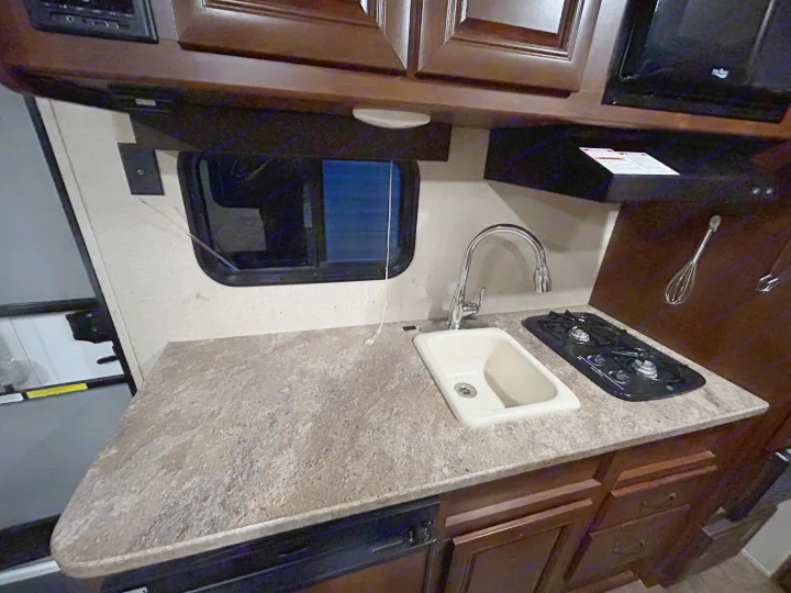 Compact RV rental kitchen featuring a sink, two-burner stovetop, dark wood cabinets, and a window.. Crossroads RV Z-1 Lite 2017