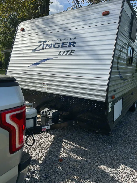 A Zinger Lite travel trailer, ideal for RV rental adventures, hitched to a truck on gravel. Features propane tanks.. Crossroads RV Z-1 Lite 2017