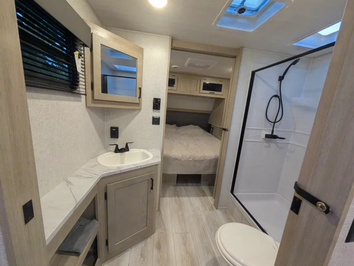 Modern rv rental interior, showcasing a sleek bathroom with shower, toilet, sink, and a cozy bedroom beyond.. Forest River Alta 2850KRL 2025